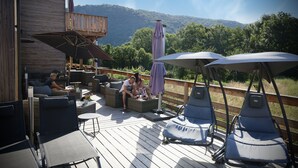 A wooden deck with outdoor seating, including sofas and lounge chairs, overlooking a mountainous landscape. - Le Volcans des Sens (Torsiac)