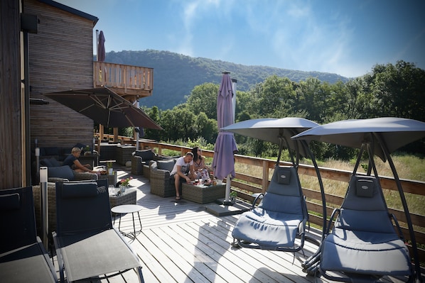 A wooden deck with outdoor seating, including sofas and lounge chairs, overlooking a mountainous landscape. - Le Volcans des Sens (Torsiac)