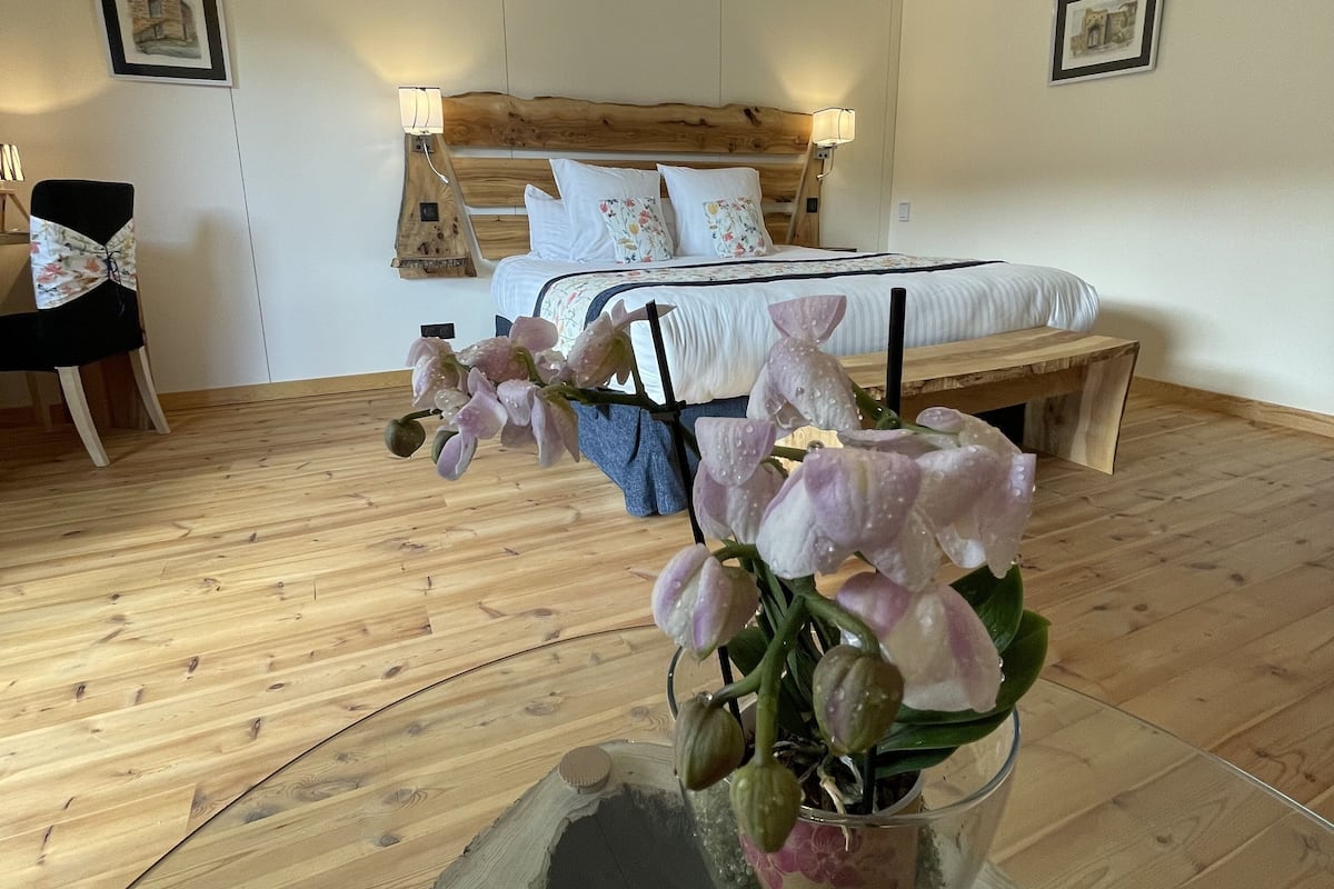 A bedroom with a wooden floor, a bed with white bedding, a nightstand, and a chair.