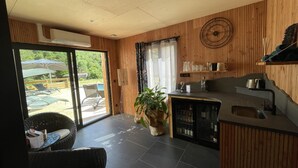 A modern kitchen with a wooden interior, a dining area with a table and chairs, and a view of an outdoor deck with umbrellas. - Le Volcans des Sens (Torsiac)