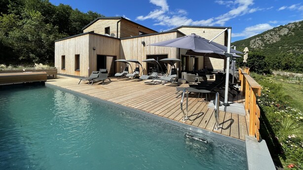 A wooden deck with a pool, lounge chairs, and umbrellas. - Le Volcans des Sens (Torsiac)