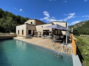 A wooden deck with a pool, lounge chairs, and umbrellas. - Le Volcans des Sens (Torsiac)