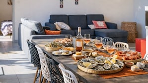 A dining table set with seafood, wine, and glasses in a modern living room with a sofa and a crossword puzzle on the wall. - Family villa with pool – 6 guests (Les Sables-d´Olonne)