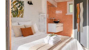 A bedroom with a bed, white bedding, a towel stack, a bedside lamp, a wall-mounted cabinet, and a window. - Family villa with pool – 6 guests (Les Sables-d´Olonne)