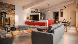A modern living room with a fireplace, grey sofas, a red kitchen island, and a dining area with a wooden table and chairs. - Family villa with pool – 6 guests (Les Sables-d´Olonne)