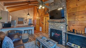 A cozy cabin interior with a stone fireplace, wooden walls, a bar area, and a comfortable seating area. - Rustic Retreat in the Smokies (Sevierville)