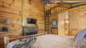 A wooden cabin room with a bed, a fireplace, a ceiling fan, and a mounted TV. - Rustic Retreat in the Smokies (Sevierville)