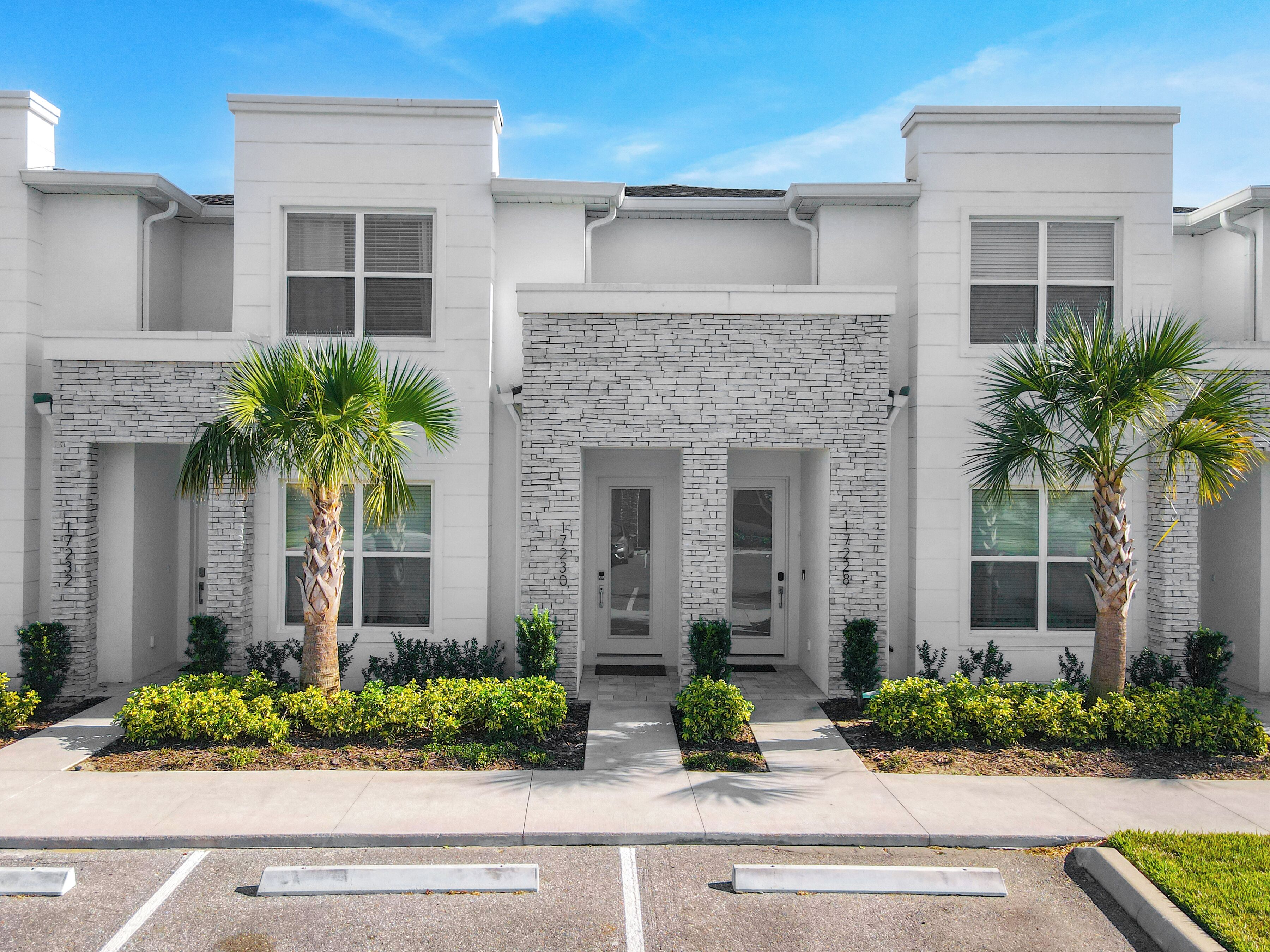 A modern building with a stone facade, two palm trees, and a parking lot.