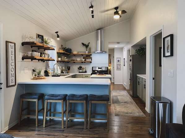 A modern kitchen with wooden bar stools, a central island, and open shelving.