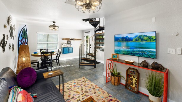 A modern living room with a black leather sofa, a colorful rug, a large flat-screen TV, and a staircase leading to a loft area. - 1- King bed/ 1- sofa bed/ 1.5bath Block from Beach (Cocoa Beach)