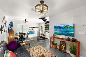 A modern living room with a black leather sofa, a colorful rug, a large flat-screen TV, and a staircase leading to a loft area. - 1- King bed/ 1- sofa bed/ 1.5bath Block from Beach (Cocoa Beach)