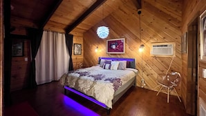 Une chambre confortable, aménagée dans un chalet en bois, avec un lit, un ventilateur de plafond et un climatiseur fixé au mur.