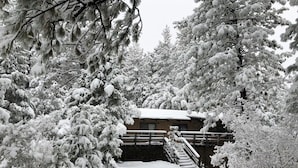 Un chalet enneigé, avec un escalier en bois menant à une entrée abritée.