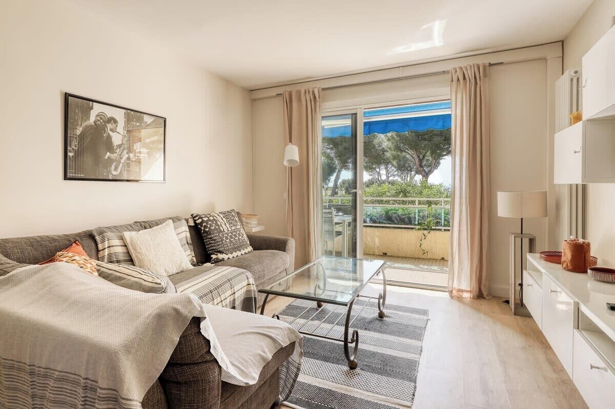 A modern living room with a sofa, a glass coffee table, and a view of a balcony with outdoor furniture.