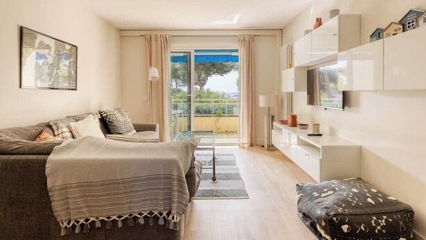 Ein modernes Wohnzimmer mit Sofa, Couchtisch und Fernseher. Ein Balkon bietet Blick ins Freie.