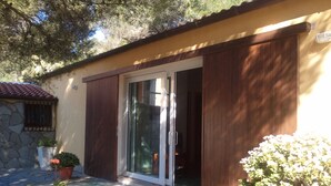 Une maison avec une façade en pierre, un toit en tuiles et une porte-fenêtre coulissante. Des plantes en pot sont disposées devant la maison.