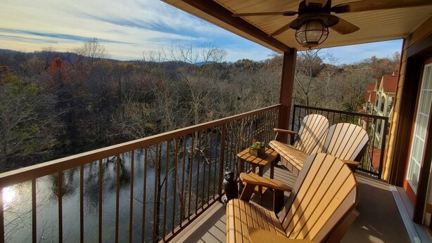 Eine Holzterrasse mit Adirondack-Stühlen und einem Tisch, mit Blick auf einen Fluss und einen bewaldeten Bereich.