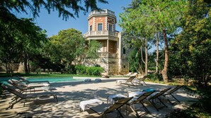 A pool area with lounge chairs, a stone tower, and surrounding greenery. - Villa Rosa Resort - House 9 (Conversano)