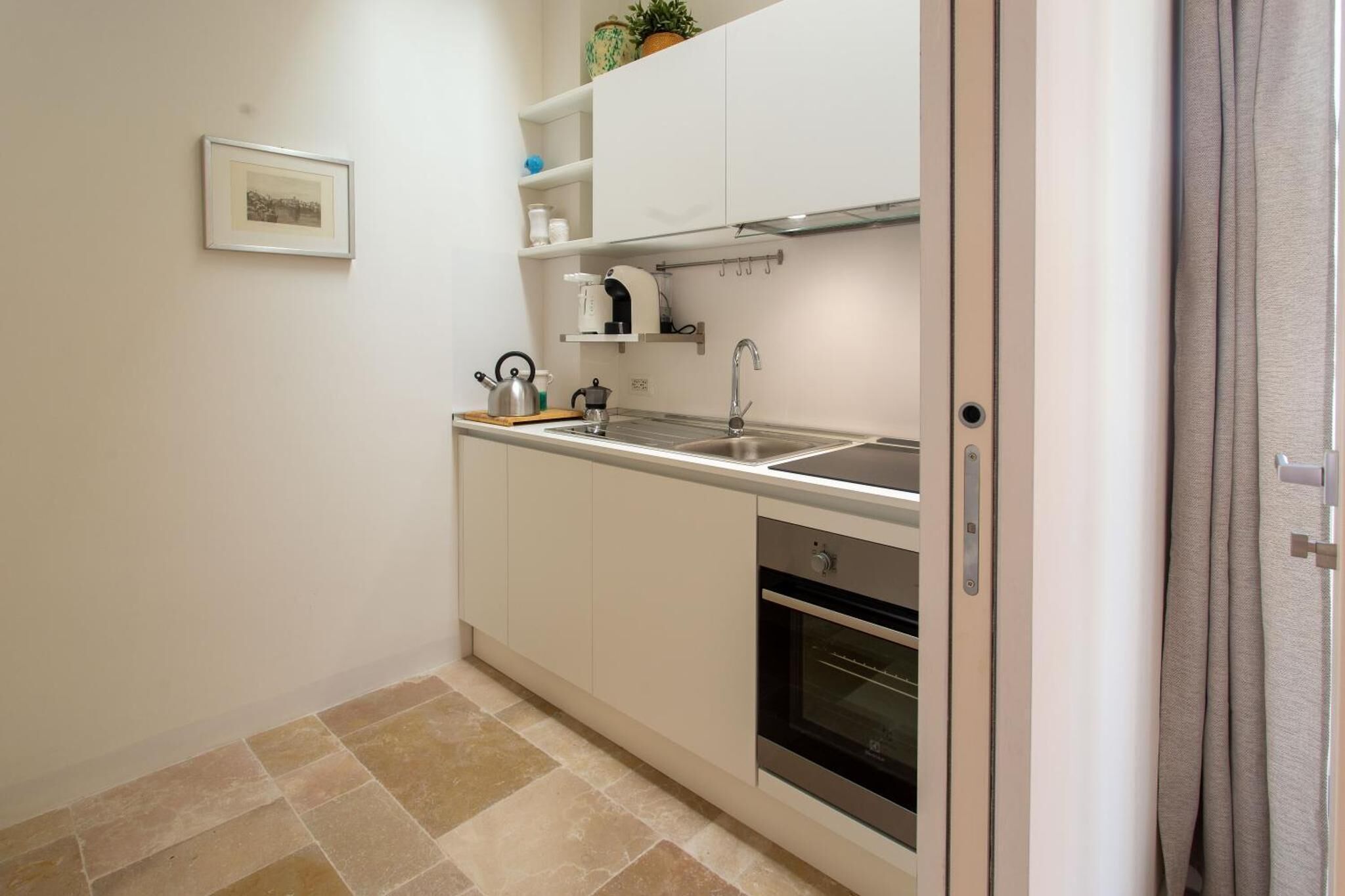 A compact kitchen with white cabinets, a stainless steel sink, and a built-in oven.