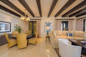 A spacious living area with a round dining table, yellow chairs, a beige sofa, and a chandelier.