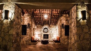Una habitación con paredes de piedra, una chimenea, dos sofás y suelo de baldosas.