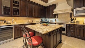 Una cocina con armarios de madera oscura, encimera de granito y una isla central con dos sillas rojas.