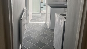 A narrow hallway with a tiled floor leading to a kitchen area with white cabinets and a built-in oven. - Spacious 1-bed Apartment in the Heart of Herne Bay (Herne Bay)
