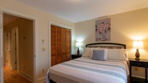 A bedroom with a bed, a nightstand, a lamp, a wooden closet, and a painting on the wall. - Heart of Downtown Bar Harbor - fully airconditioned (Bar Harbor)