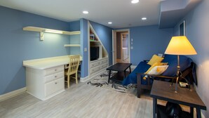 A compact room with a kitchenette, a bed with a blue headboard, a desk with a lamp, and a chair. - Heart of Downtown Bar Harbor - fully airconditioned (Bar Harbor)