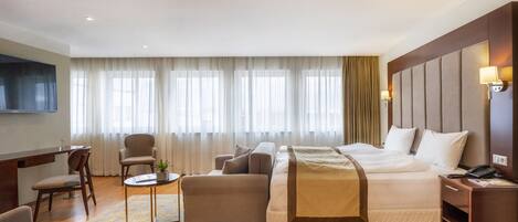 A hotel room with a large bed, a desk, a sofa, and a TV.
