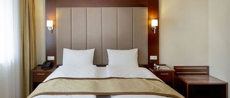 Una habitación de hotel con una cama grande, dos mesitas de noche, una lámpara de pared y una silla de madera.