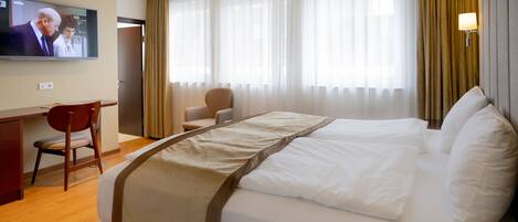 Une chambre d’hôtel avec un lit, un bureau, une chaise, une télévision et des rideaux.