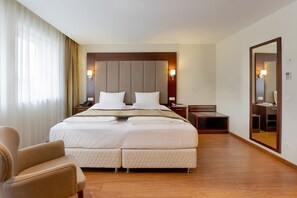 Une chambre d’hôtel avec un grand lit, une chaise, une table de chevet, un miroir et une fenêtre avec des rideaux.