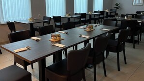 Un salón de conferencias con varias mesas y sillas, ventanas amplias con persianas y detectores de humo instalados en el techo.