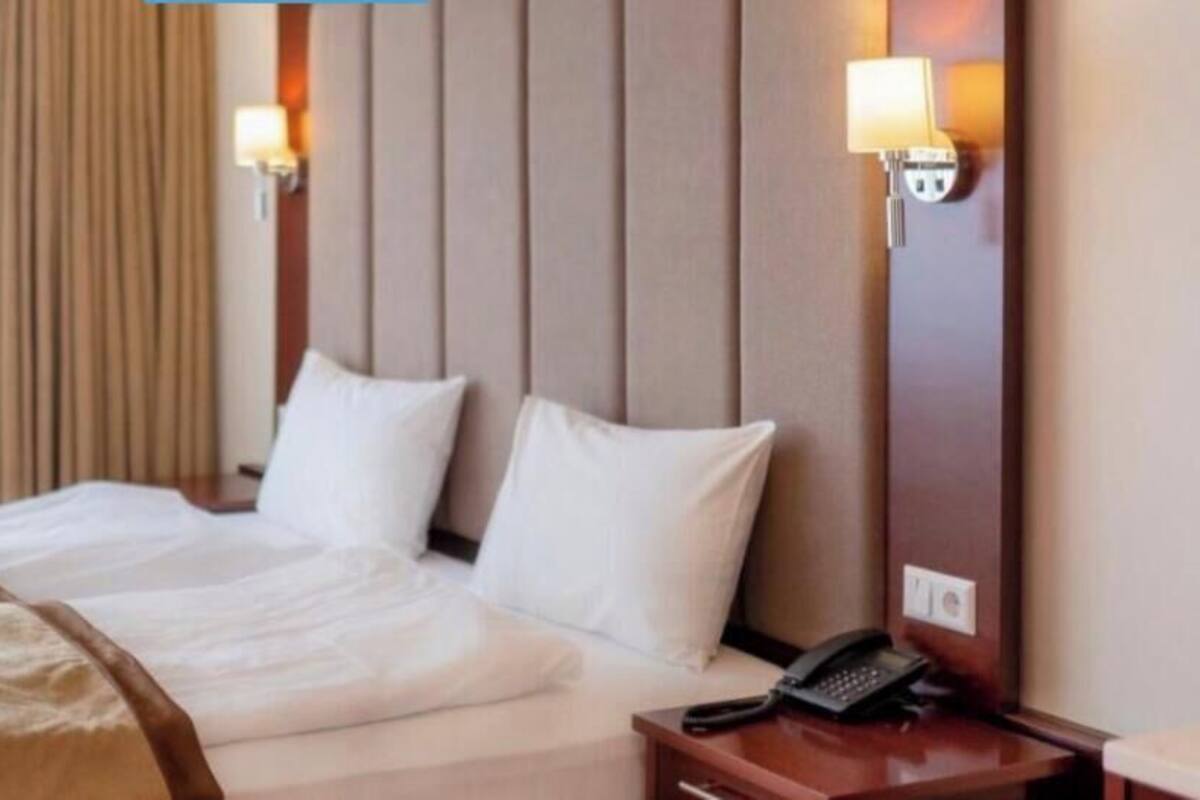 Et hotelværelse med en seng, to sengeborde med lamper, en telefon og et vindue med gardiner.