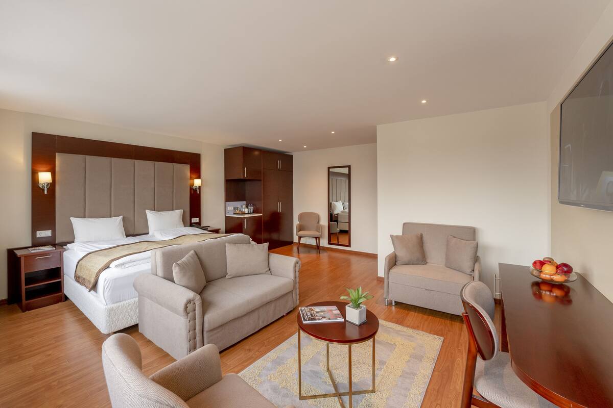 Et moderne hotelværelse med en stor seng, to sofaer, et spisebord og et lille sofabord.