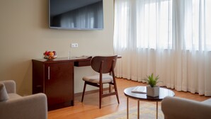 Una sala moderna con un televisor de pantalla plana en la pared, un escritorio de madera con una silla, una mesita redonda con una planta y un sofá.