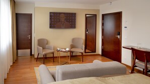Una habitación de hotel con dos camas individuales, una mesita con una silla, dos sillones y un cuadro en la pared.