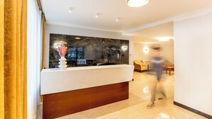 Una moderna zona de recepción con mostrador de mármol, un florero con flores secas y un panel de madera.