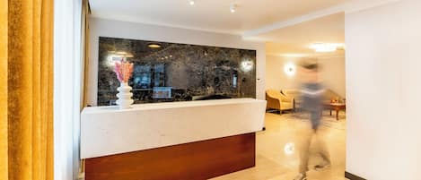Una moderna zona de recepción con mostrador de mármol, un florero con flores secas y un panel de madera.