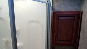 Une petite salle de bain comprenant un espace douche, des toilettes et un petit meuble en bois.