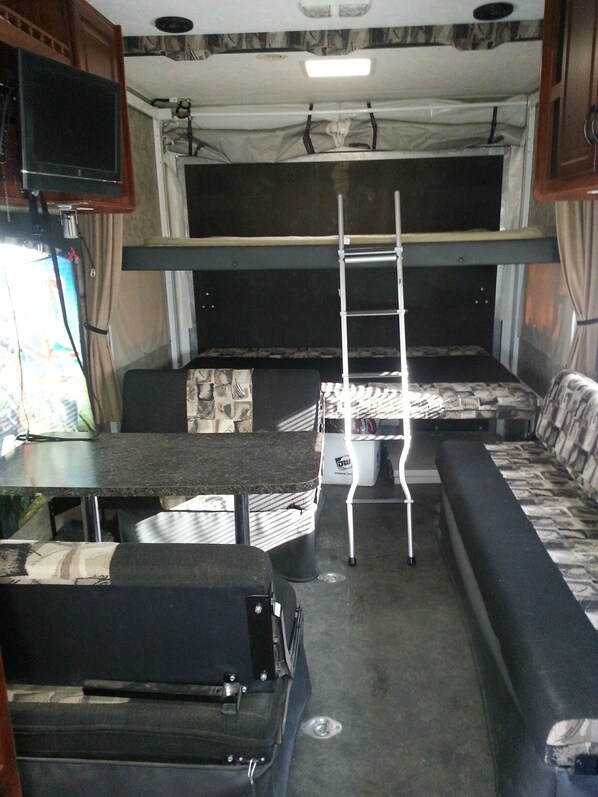 A compact RV interior with a bunk bed, a small table, and a sofa.