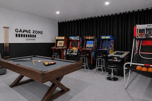 Ein Billardtisch, Spielautomaten und ein Basketballkorb in einem Raum mit schwarzem Vorhang im Hintergrund.