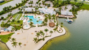 Luchtbeeld van een resort met een centraal gelegen zwembad, palmbomen en een steiger.