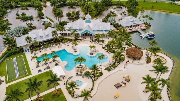 Een resort met een groot zwembad, een tennisbaan en een strand, omgeven door palmbomen.