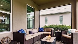 Een terras buiten met rieten meubilair, een vuurkorf en uitzicht op een huis.