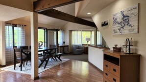 En rummelig stue med et træbord og stole, et hyggeligt opholdsområde med en stribet sofa og et træskab med skuffer.