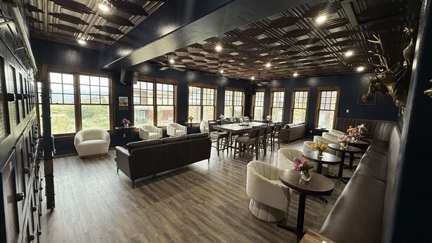A spacious room with a high ceiling, large windows, and a variety of seating arrangements including sofas and tables.