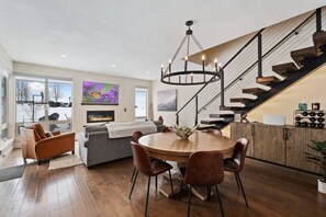 Cozy living space with a round dining table, fireplace, and staircase leading to an upper level.