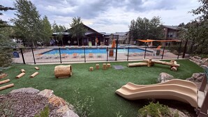 A pool area with a slide, artificial grass, and wooden logs.